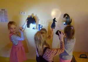 Czworo dzieci trzyma w ręku sylwety ludzi, zwierząt i roślin na które święcą latarkami tworząc cień na ścianie.